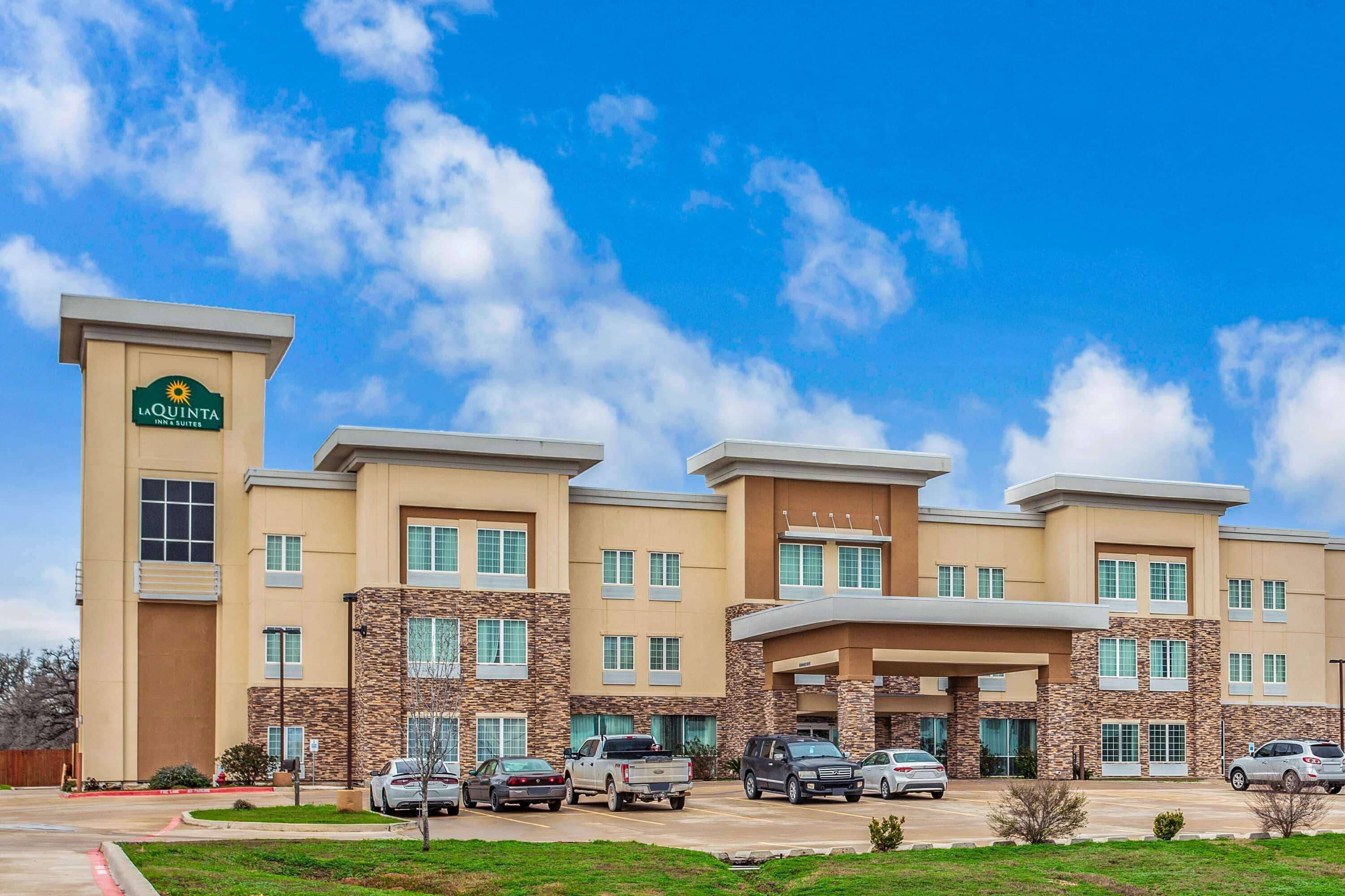 Un bâtiment de la chaîne La Quinta Inn & Suites, avec un parking et un ciel bleu dégagé.