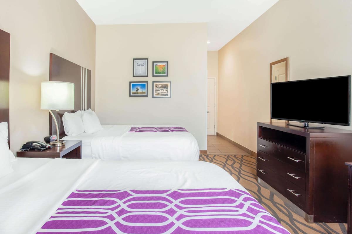 A hotel room with two beds, a TV, a desk with a lamp, and a wall with framed pictures.