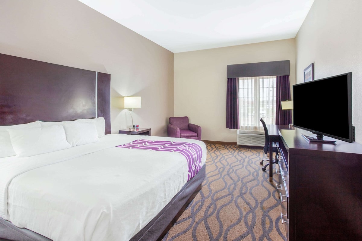 A hotel room with a large bed, a desk with a flat-screen TV, a chair, and a window with curtains.