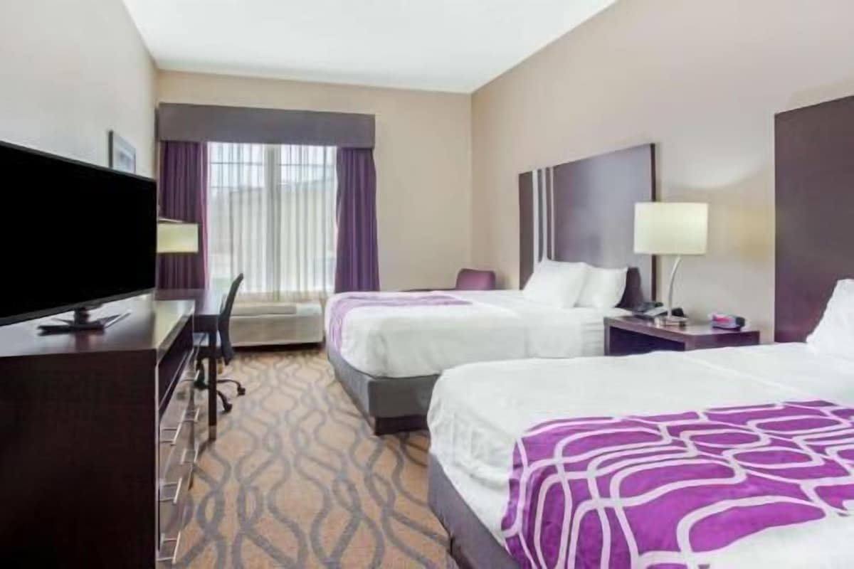 A hotel room with two beds, a desk with a TV, a chair, a lamp, and a window with curtains.