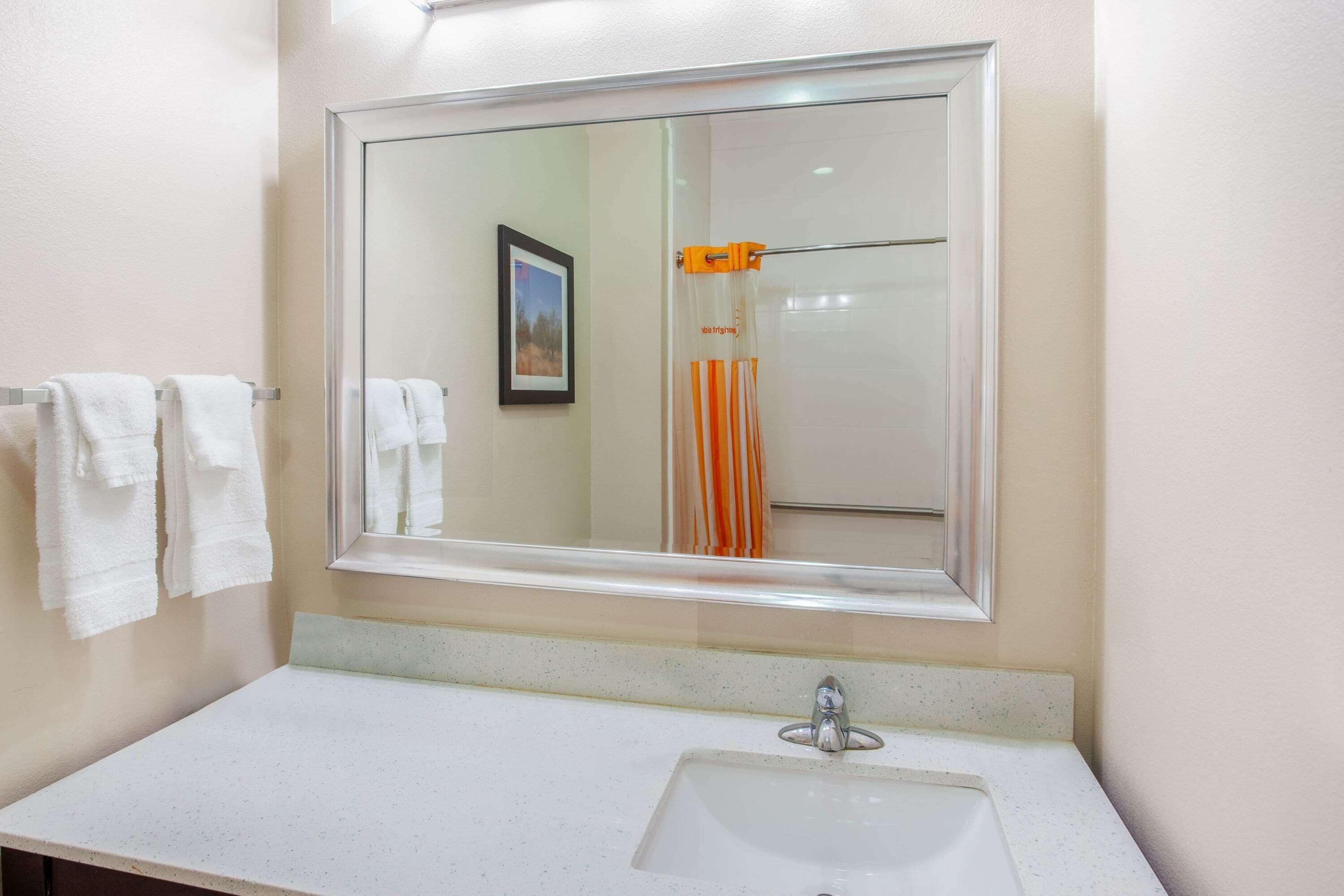 Un baño con un espejo grande, un lavabo y un perchero con toallas blancas.