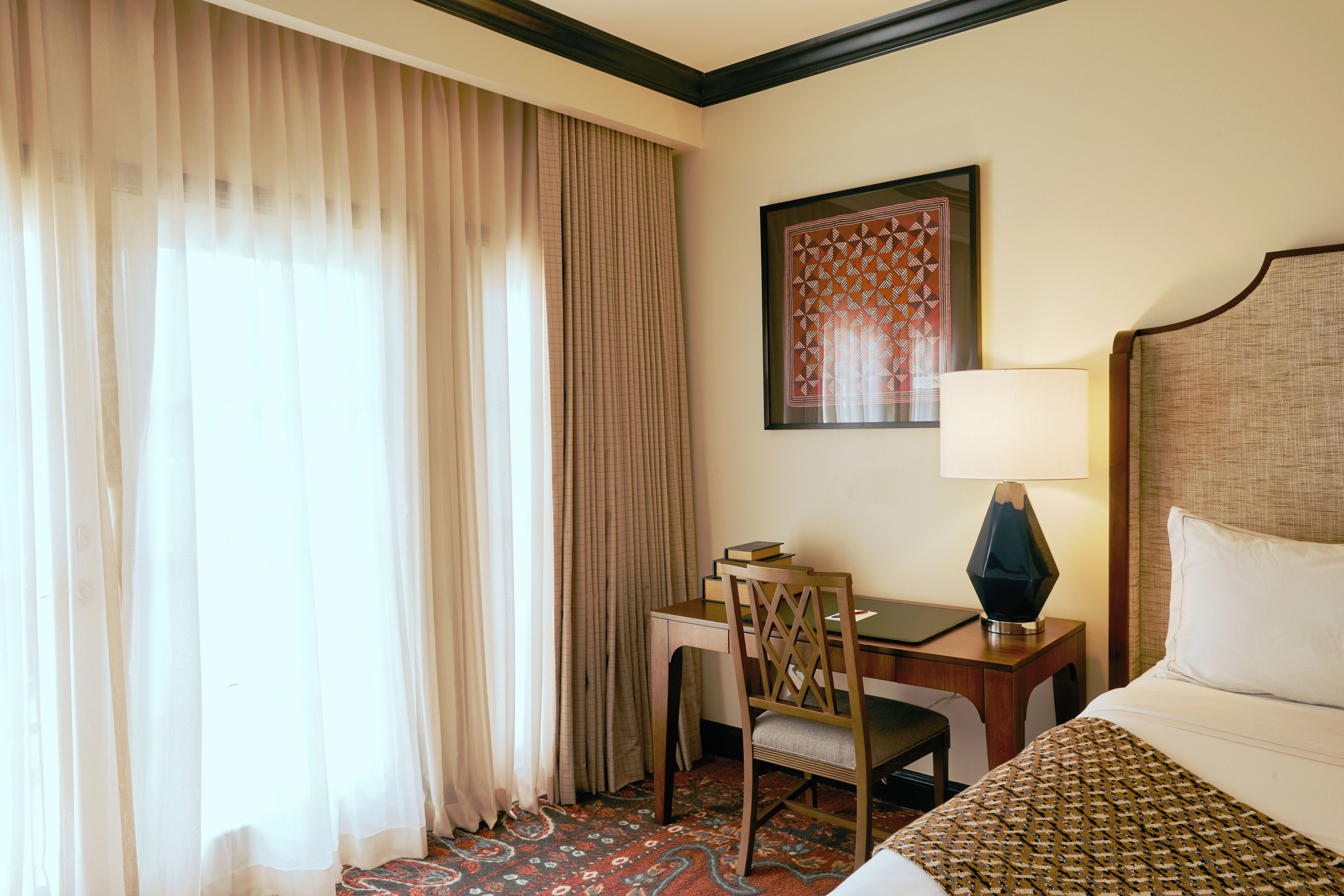 Une chambre d’hôtel avec un lit, un bureau et une chaise, une lampe et une œuvre d’art encadrée au mur.