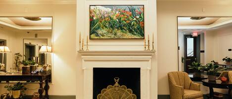 A room with a fireplace, a painting above it, and a chair to the right.