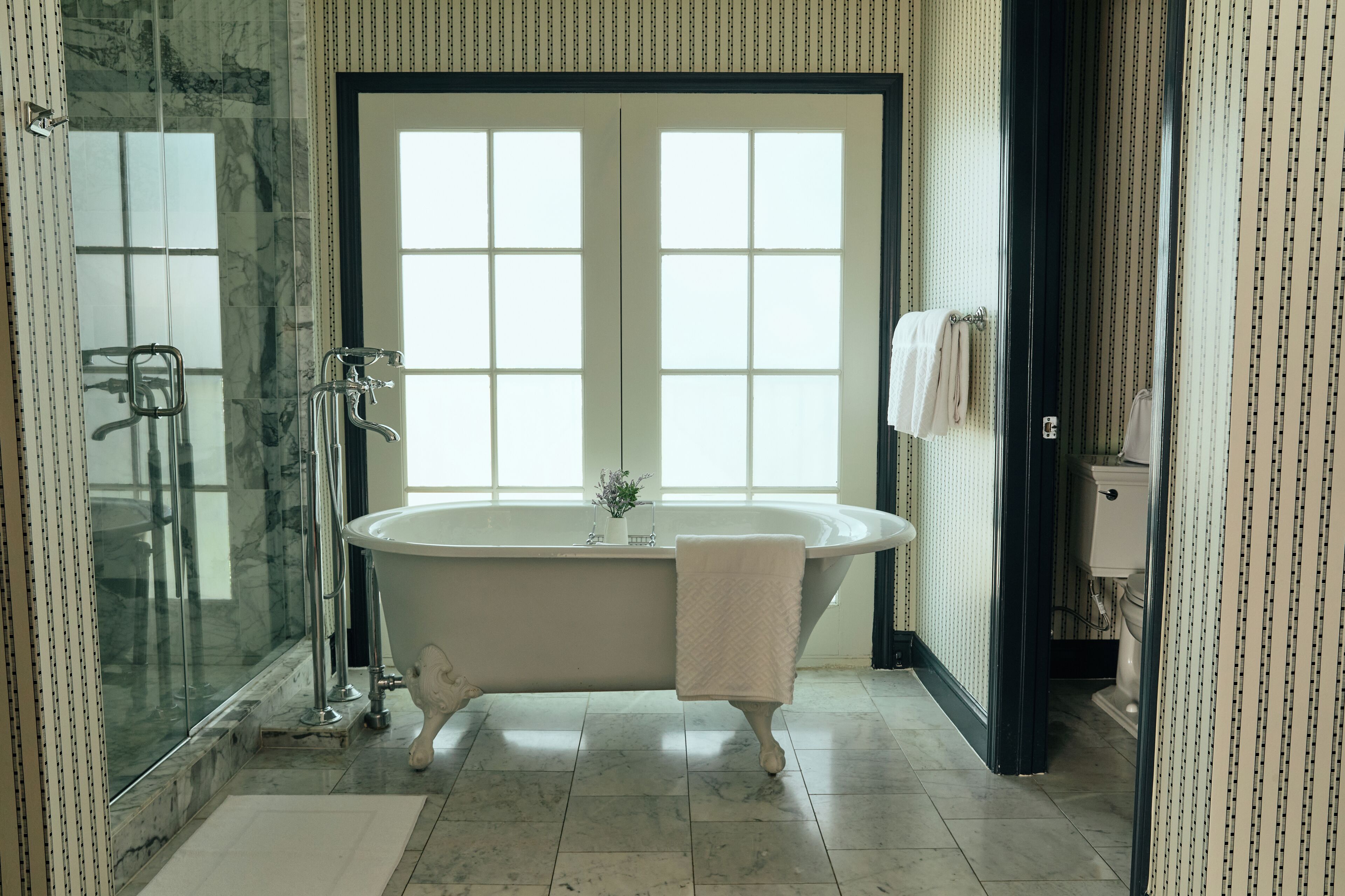 Un baño con una bañera independiente, cabina de ducha de vidrio y un ventanal grande.