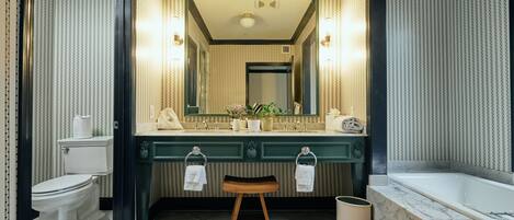 A bathroom with a large mirror, two sinks, a toilet, a wooden stool, and a bathtub.