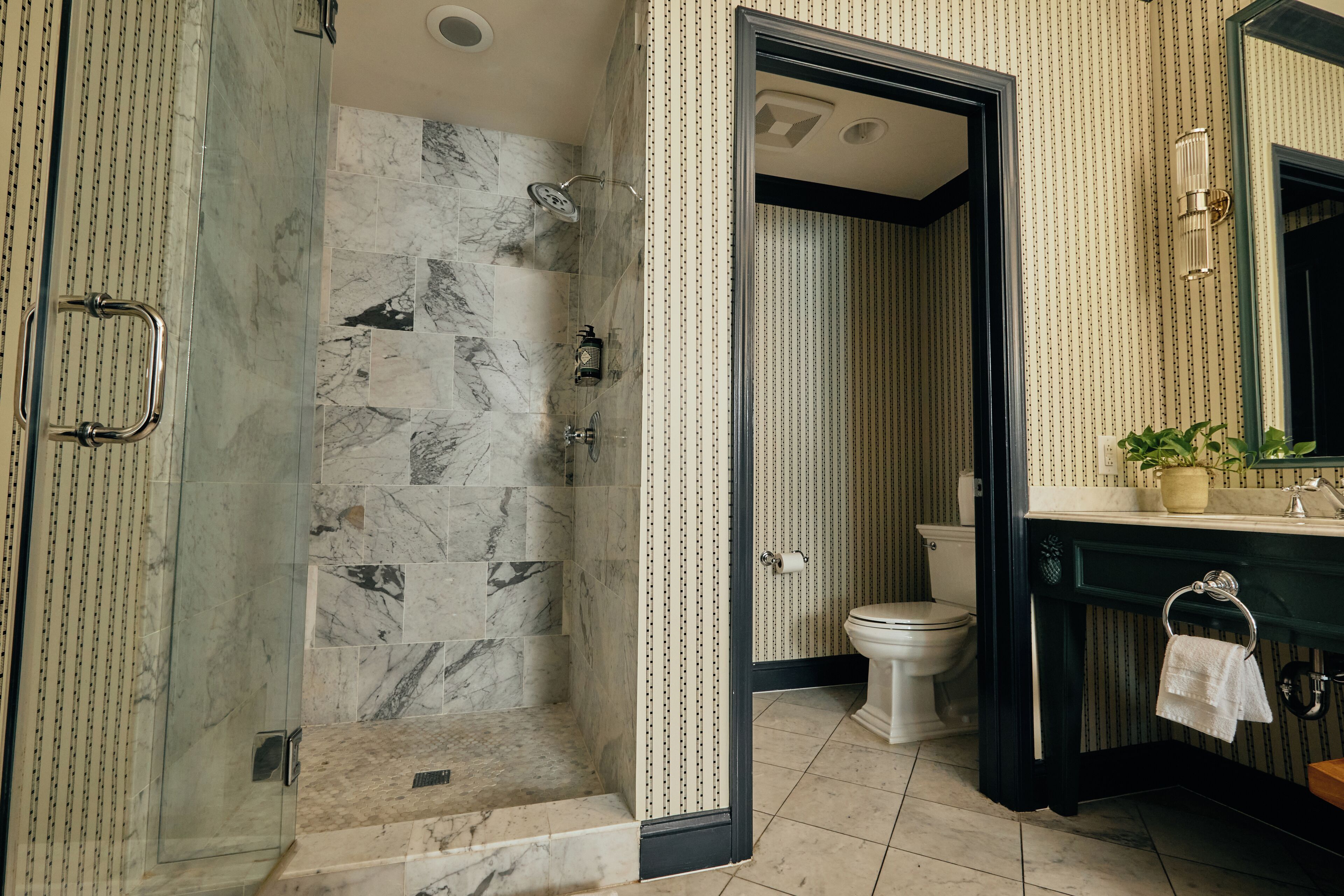 A bathroom with a glass-enclosed shower, a toilet, and a sink with a mirror.