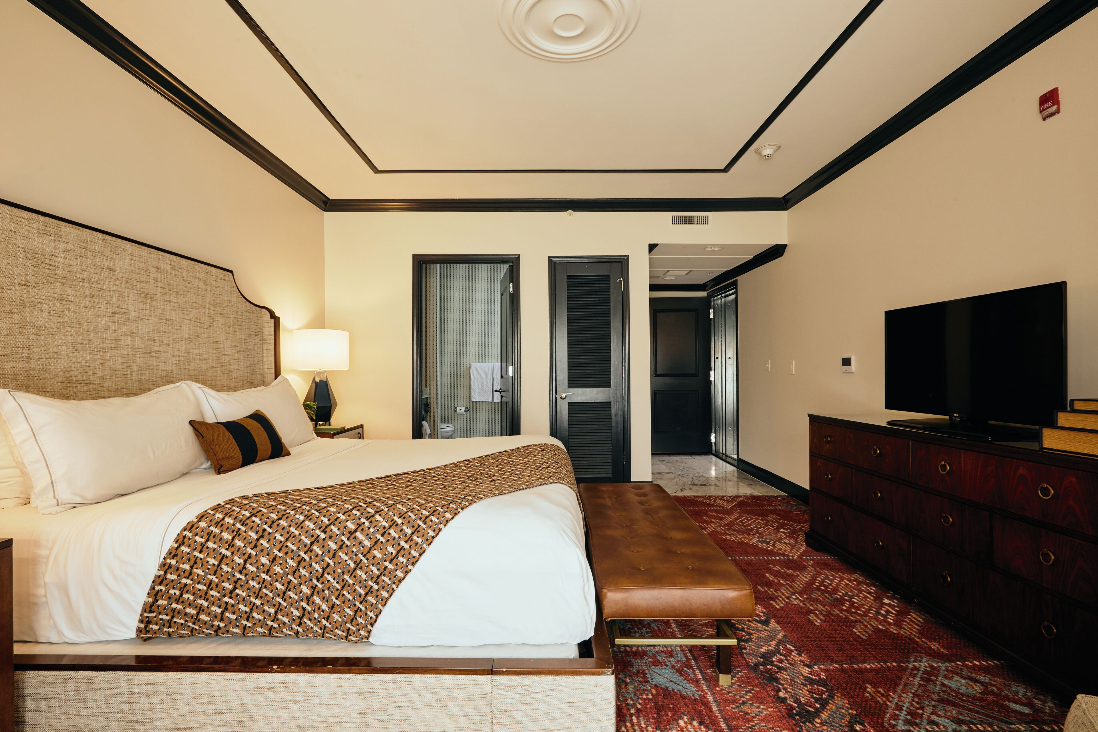 Une chambre d’hôtel avec un grand lit, un banc, une commode et un téléviseur.