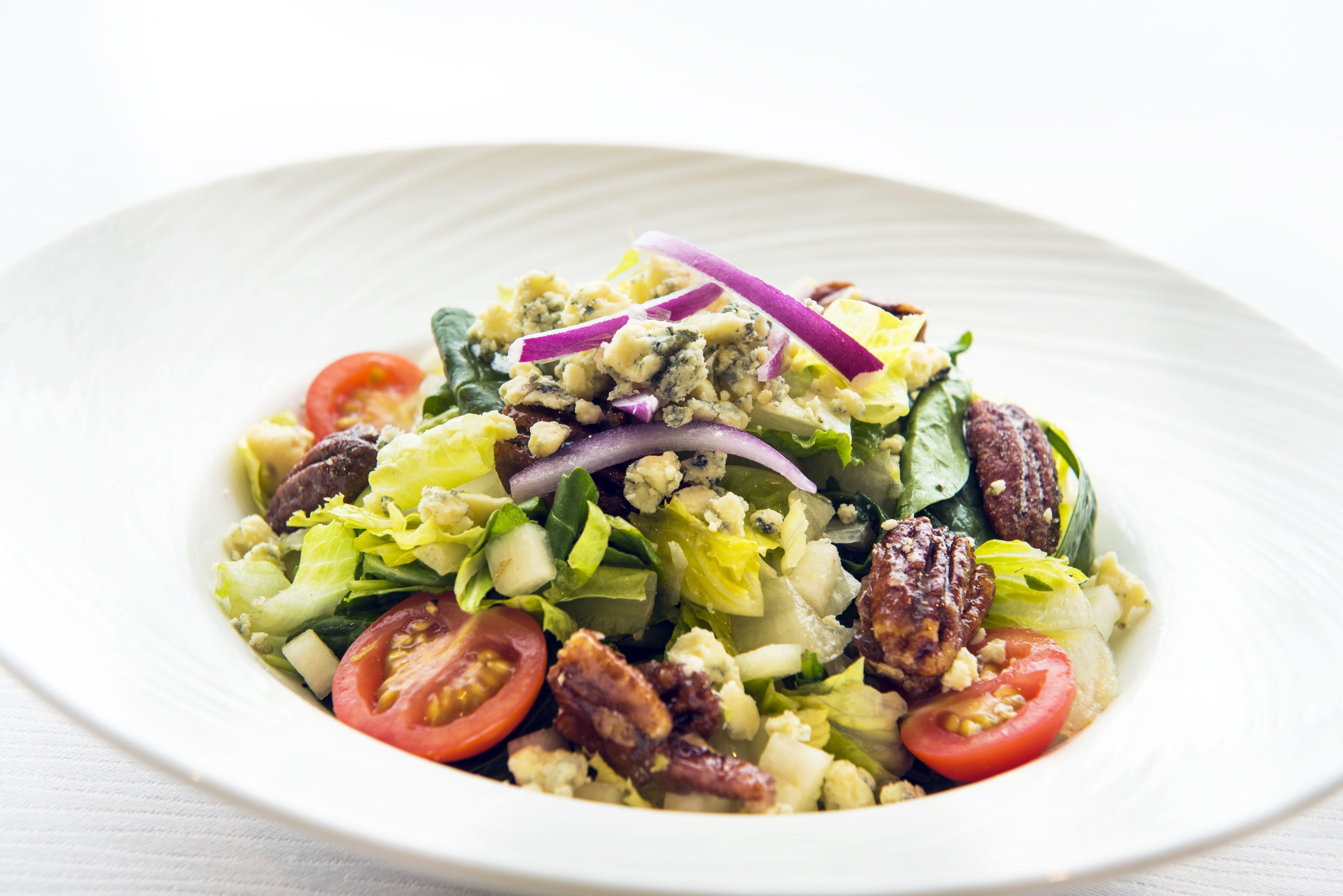 A salad with various vegetables and nuts on a white plate.