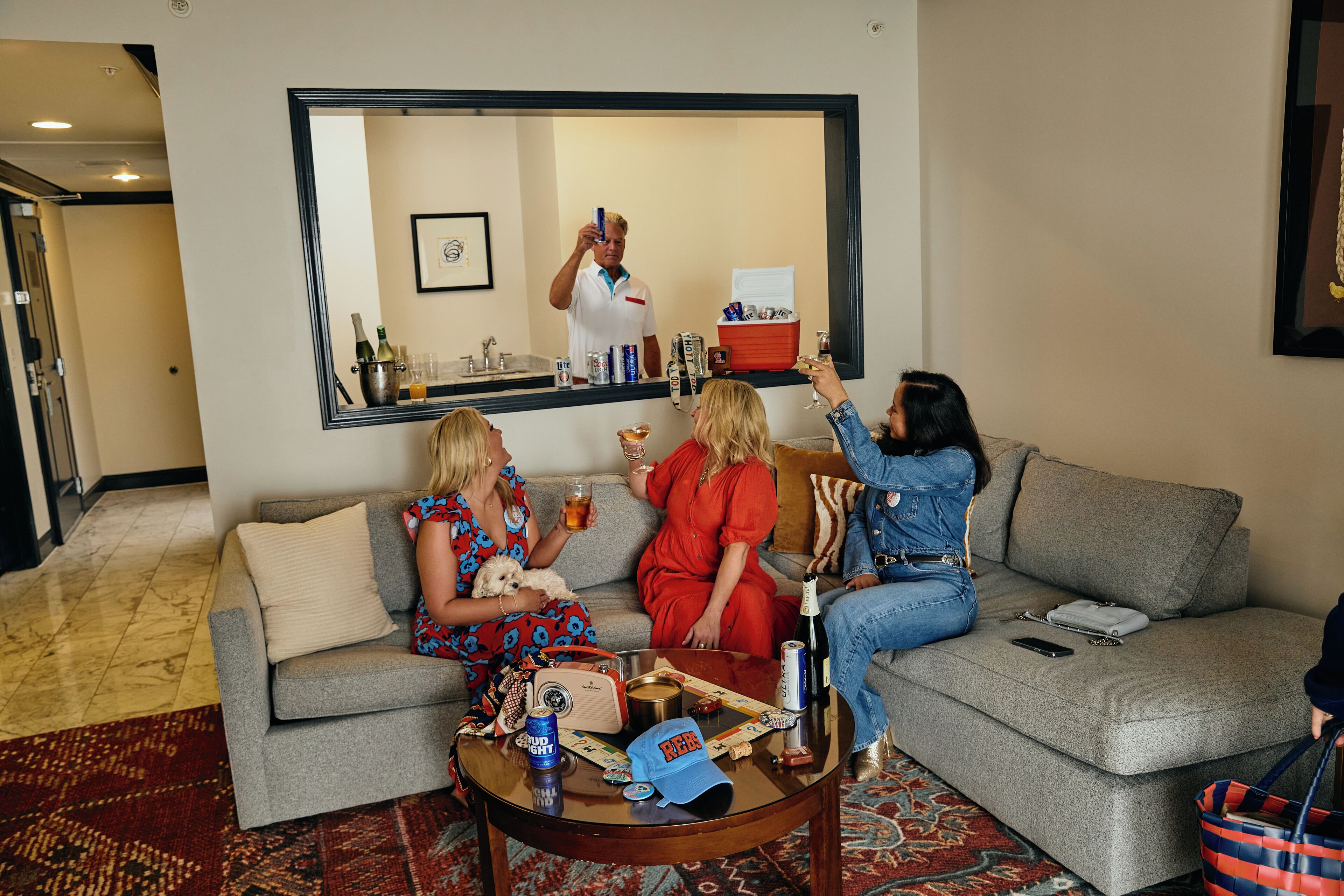A living room with a grey sofa, a coffee table with various items, and a large mirror reflecting a person taking a photo.