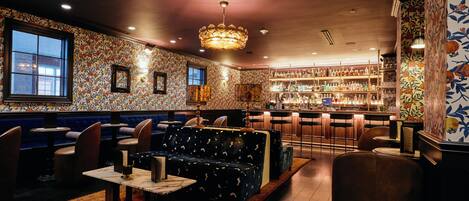 A bar area with a patterned wall, a chandelier, and a bar counter with stools.