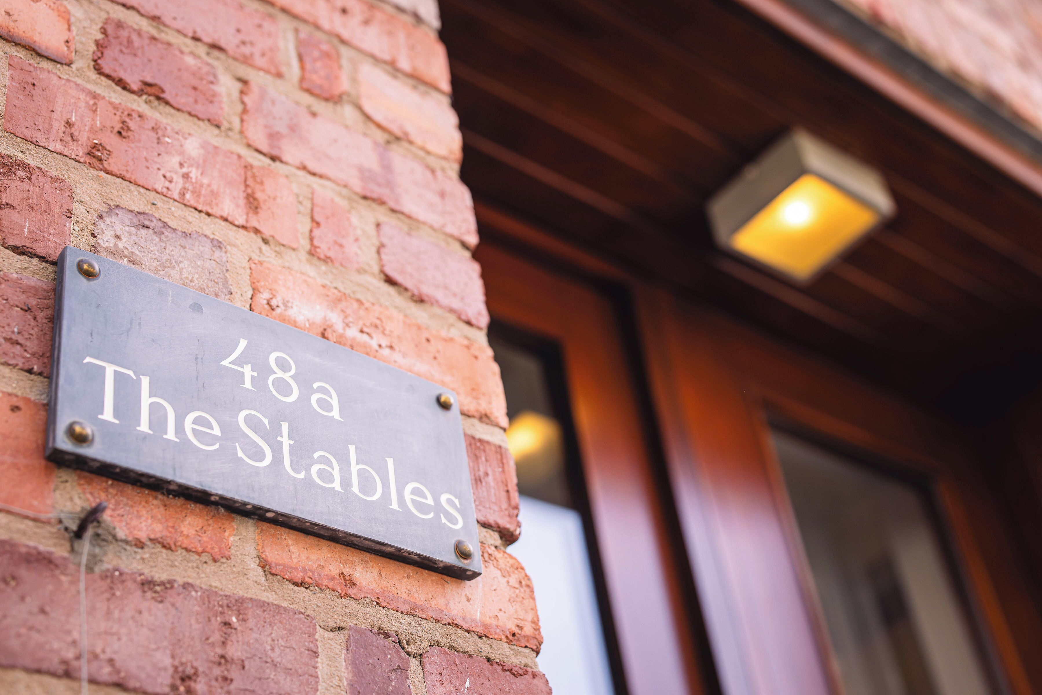 A metal sign with '48a The Stables' affixed to a brick wall.