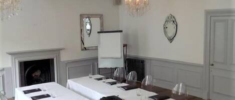 A conference room with a long table set for meetings, clear chairs, a fireplace, and chandeliers.