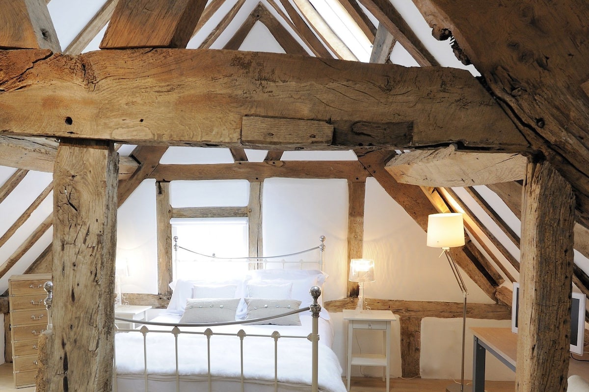 Un dormitorio con techo de madera, una cama, una mesita de noche, una silla y una lámpara.