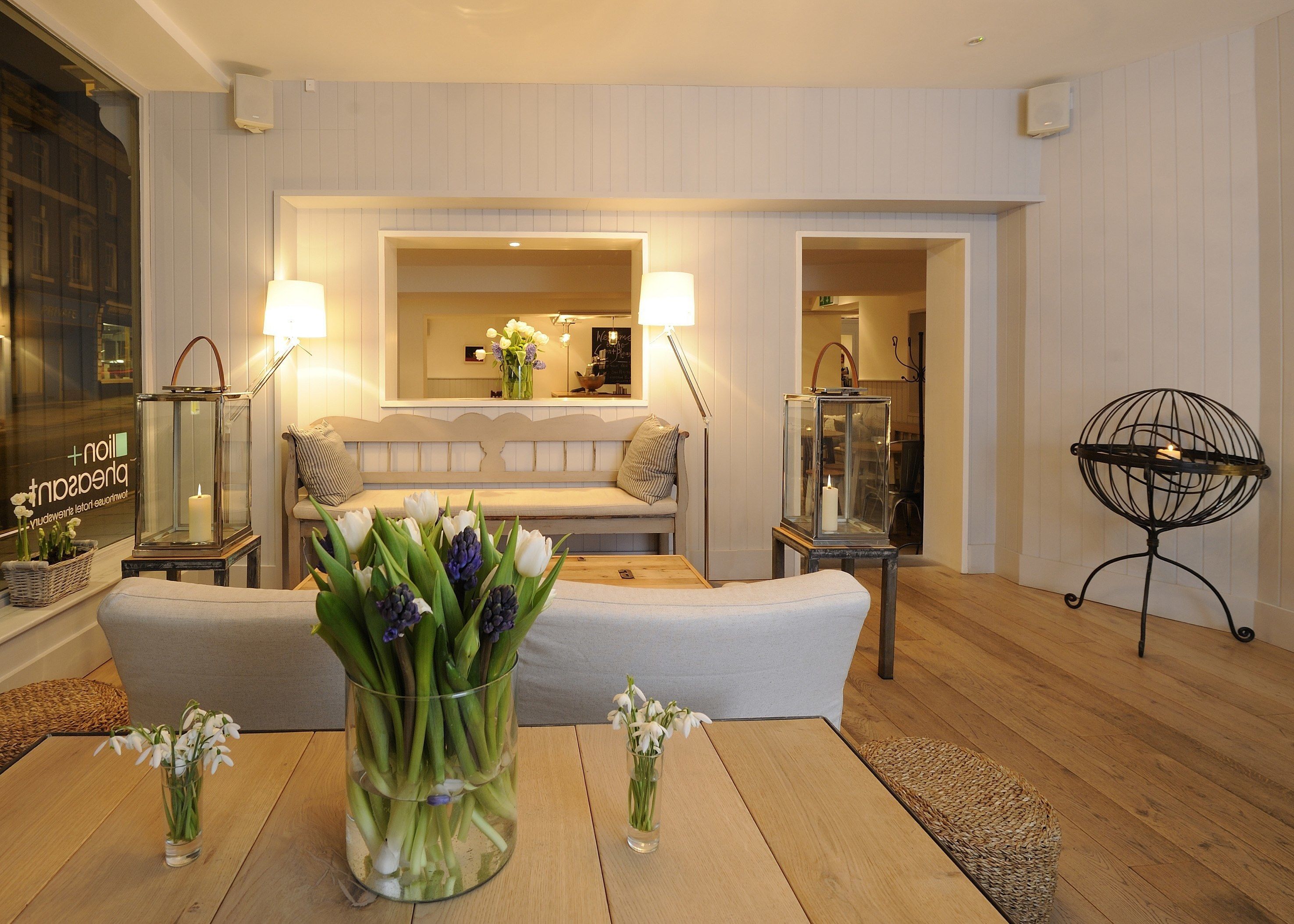 A modern living room with a sofa, a coffee table, and two side tables with lamps. There is a vase with flowers on the coffee table and another vase with flowers on one of the side tables.