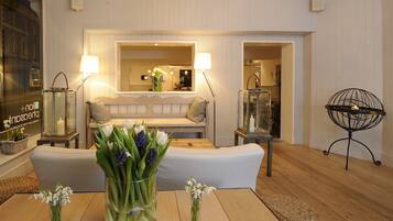 A modern living room with a sofa, a coffee table, and two side tables with lamps. There is a vase with flowers on the coffee table and another vase with flowers on one of the side tables.