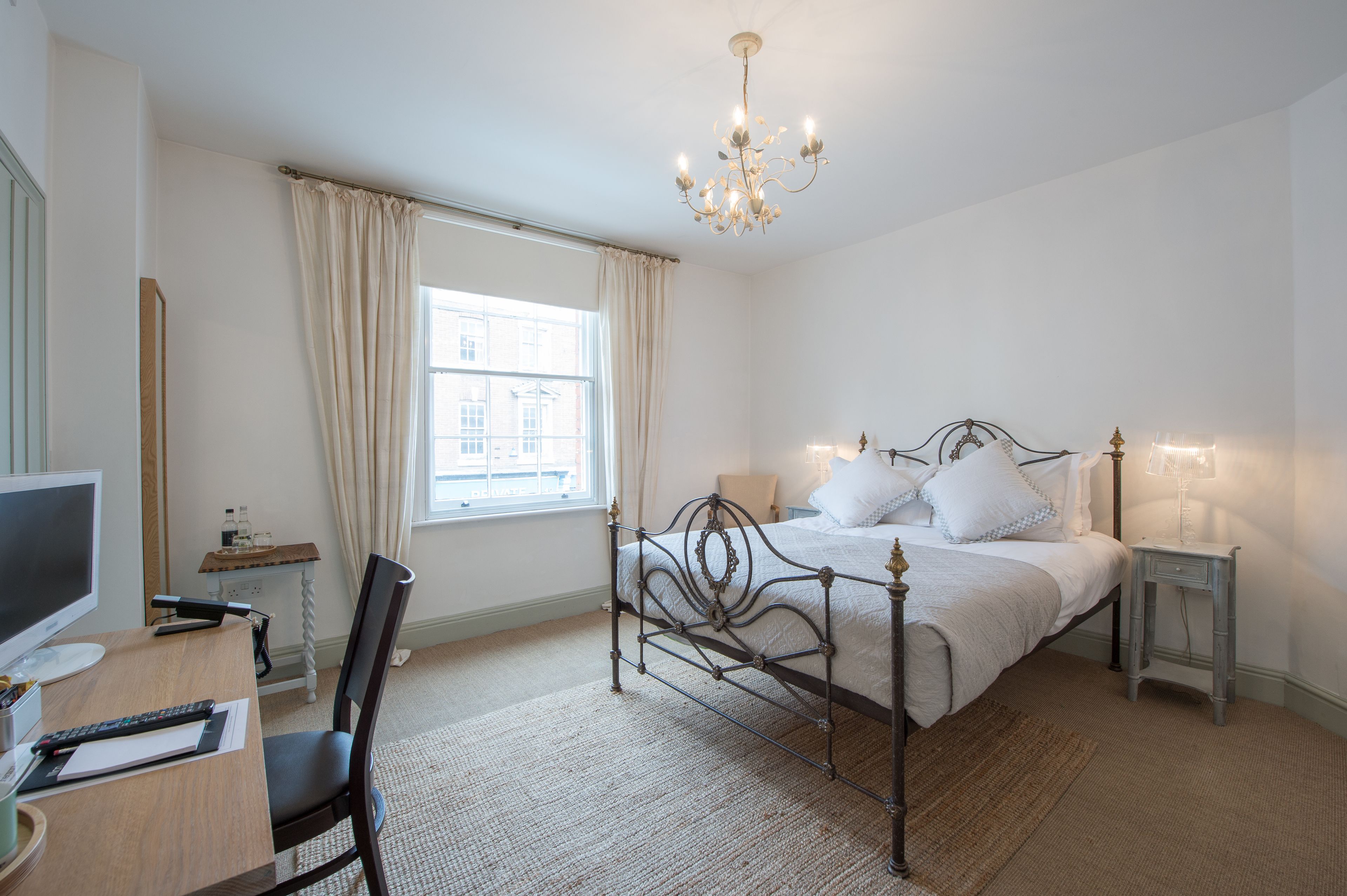 A bedroom with a bed, a desk, a chair, a TV, and a window with curtains.