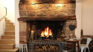 A stone fireplace with a roaring fire, a wooden staircase, and a dining area with a table and chairs. - Lion and Pheasant Hotel (Shrewsbury)