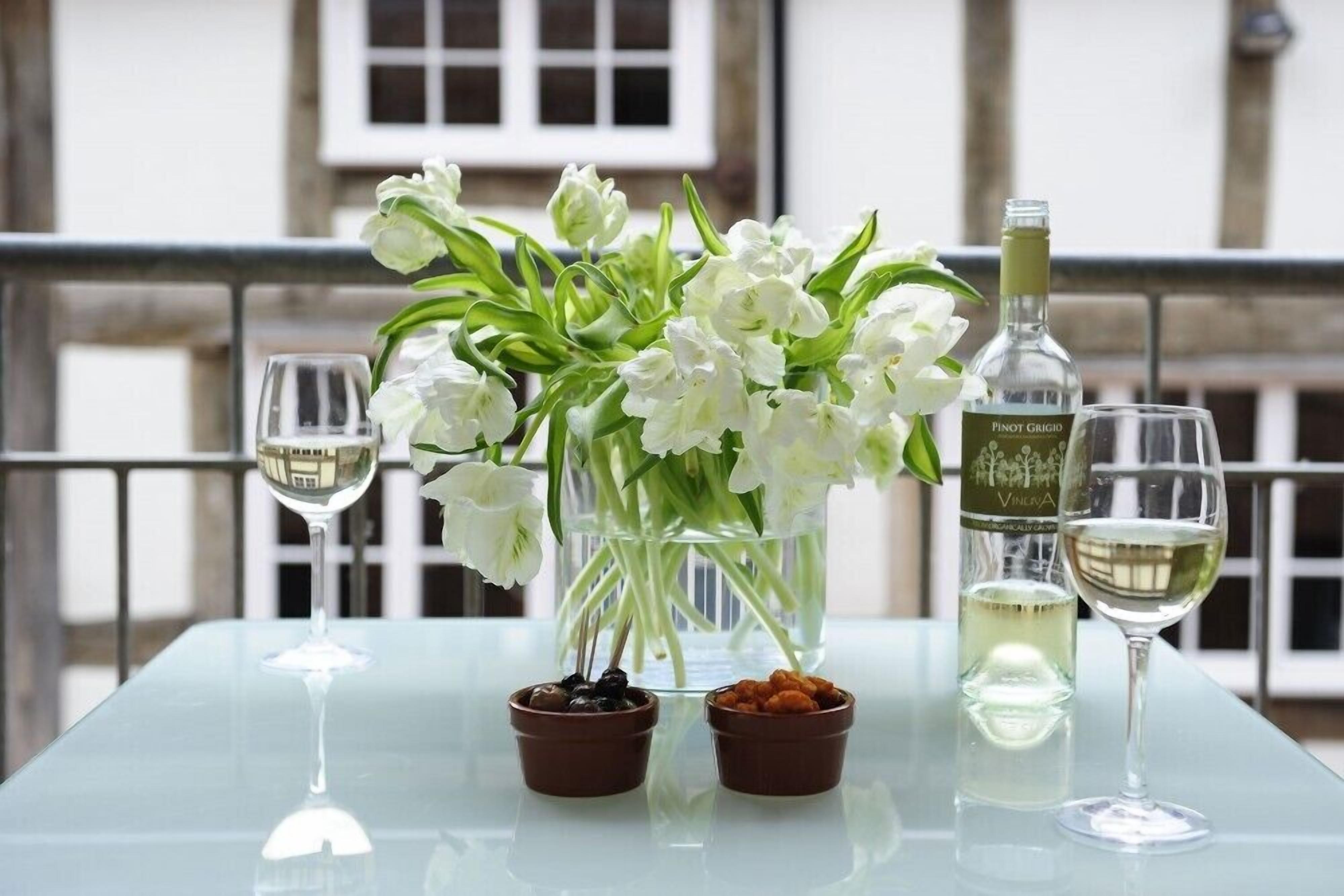 A table with two wine glasses, a bottle of Pinot Grigio, and a vase of white flowers.