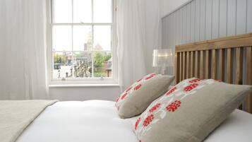 Quarto de hotel com uma cama, cortinas brancas, uma janela com vista para um edifício e uma cabeceira de madeira.