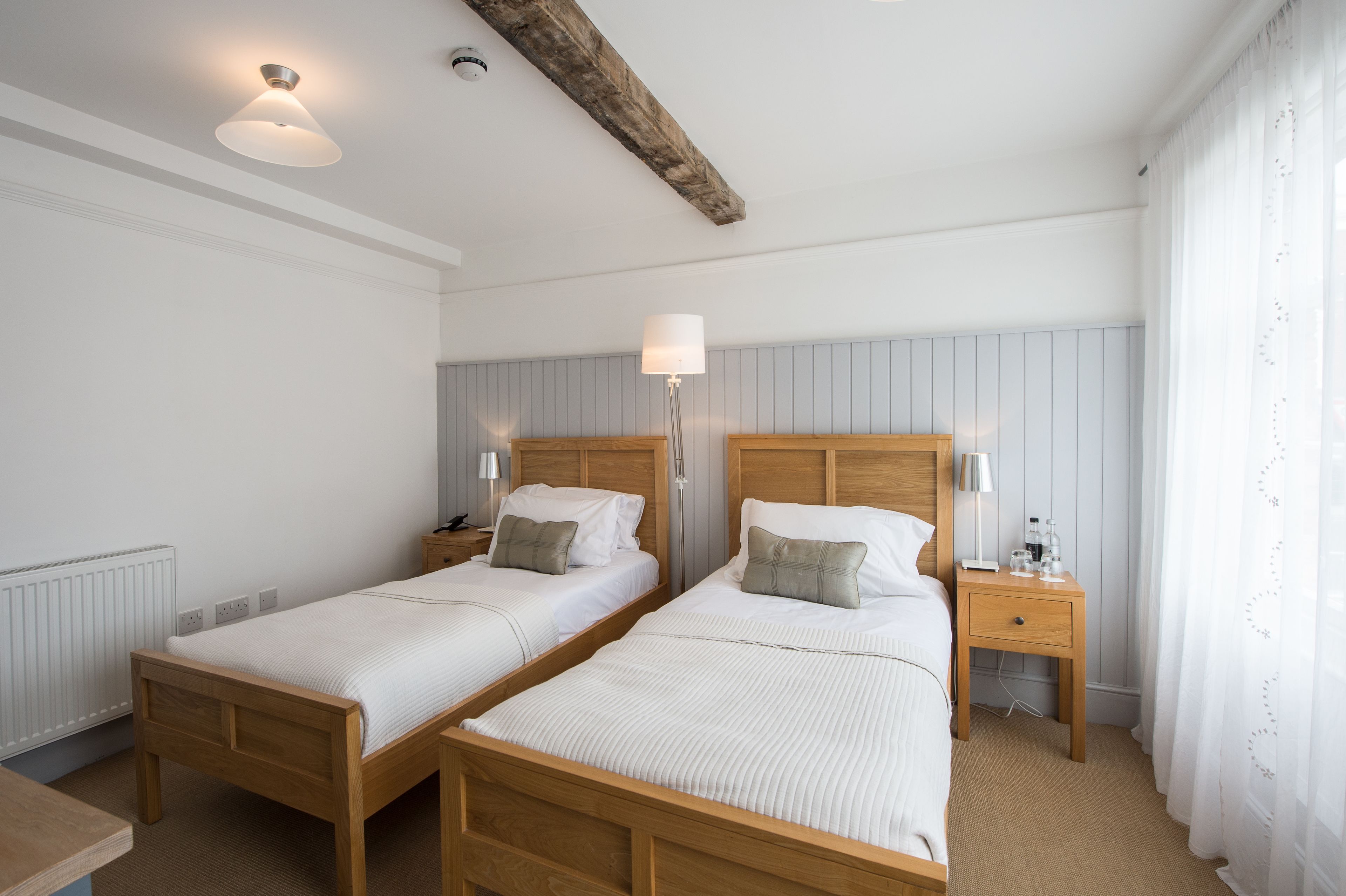 Habitación doble con dos camas, mesitas de noche, lámparas y una viga de madera en el techo.