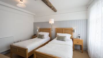 Habitación doble con dos camas, mesitas de noche, lámparas y una viga de madera en el techo.