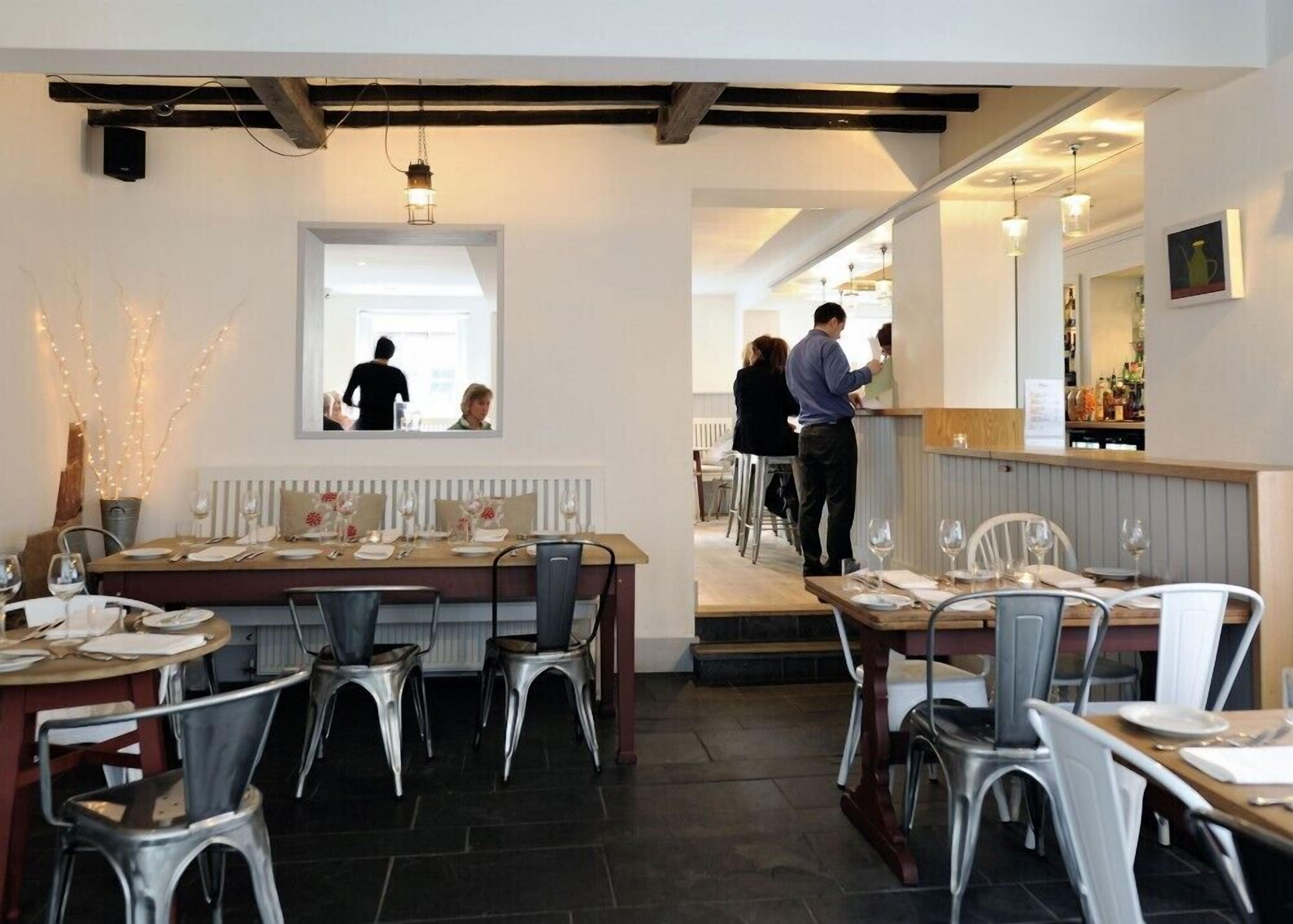 A restaurant interior with tables set for dining, a bar area, and a counter where staff are serving.