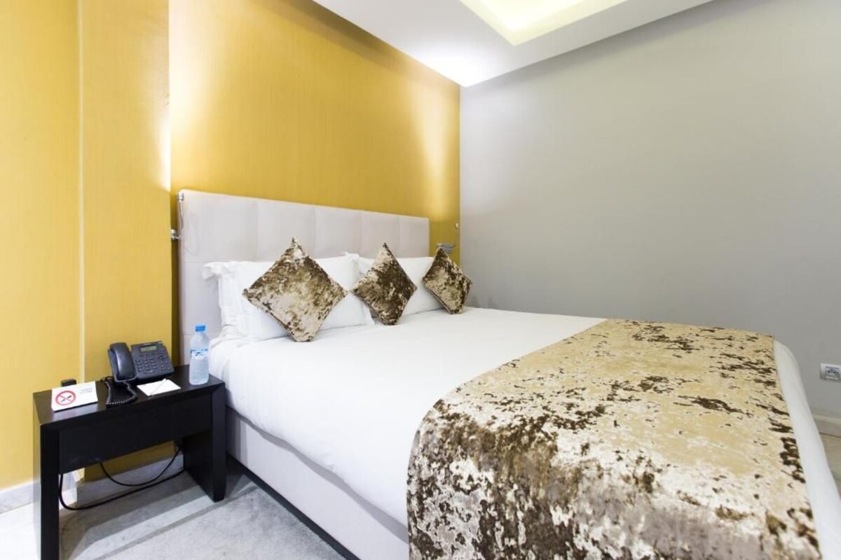A hotel room with a bed, a nightstand with a phone and a water bottle, and a sign indicating no smoking.