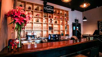 Zona de bar con estante de madera que exhibe botes y botellas varios, una máquina de café y un letrero que indica cocina italiana.