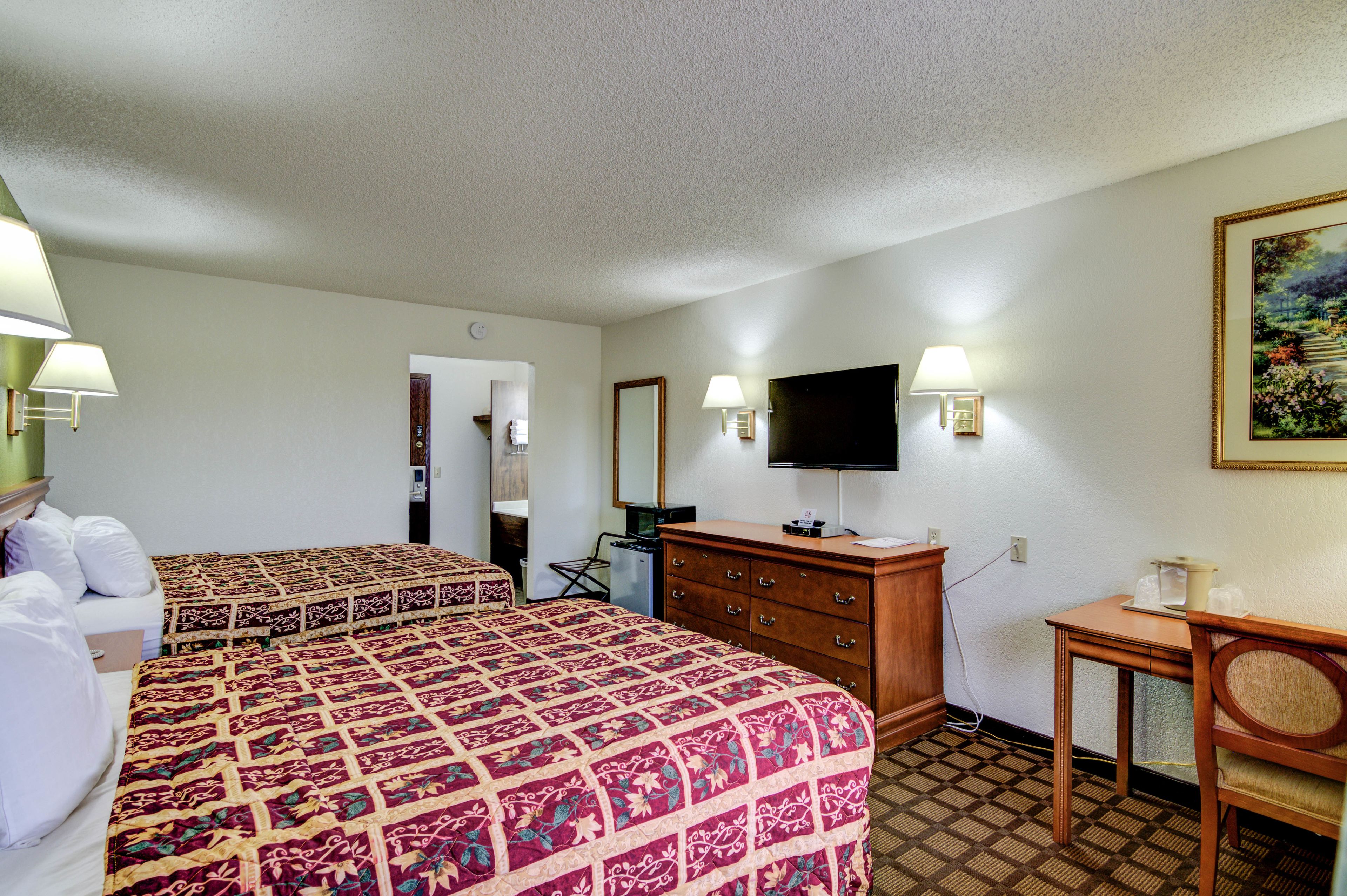 A hotel room with two beds, a television, a dresser, and a desk with a chair.