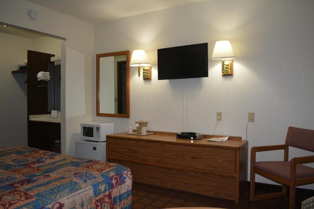 A hotel room with a bed, a wooden dresser, a television, and two wall-mounted lamps.