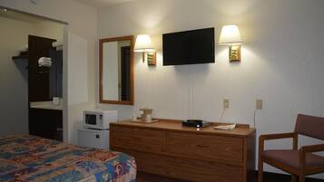 A hotel room with a bed, a wooden dresser, a television, and two wall-mounted lamps.