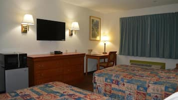 Ein Hotelzimmer mit zwei Betten, einem Schreibtisch, einem Schminktisch, einem Fernseher und einem Fenster mit Vorhängen.