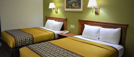 Una habitación de hotel con dos camas, cada una con cabecero de madera, ropa blanca de cama y colcha estampada. Hay lámparas de pared y un cuadro sobre las camas.