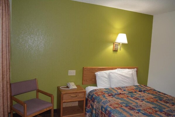 A hotel room with a single bed, a bedside table with a lamp, a chair, and a telephone. - Bloomer Inn & Suites (Bloomer)