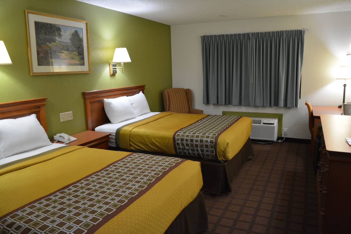 Ein Hotelzimmer mit zwei Betten, einem Schreibtisch, einem Stuhl, einem Fenster mit Vorhängen und einer Wand-Klimaanlage.