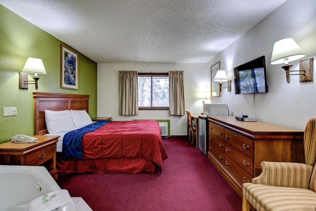 A hotel room with a bed, a desk, a chair, a TV, and a window with curtains.