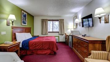 A hotel room with a bed, a desk, a chair, a TV, and a window with curtains.