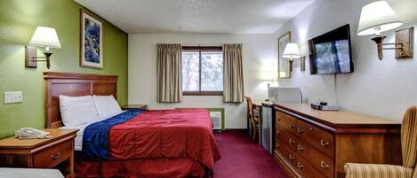 A hotel room with a bed, a desk, a chair, a TV, and a window with curtains.