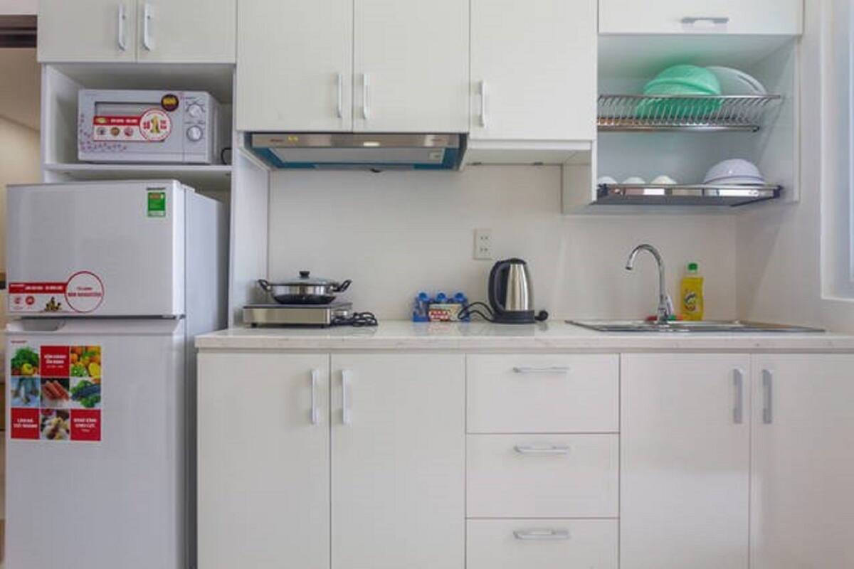 A compact kitchen with white cabinets, a microwave, a kettle, and a sink.