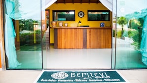 Un espace d’accueil avec un comptoir en bois, des portes vitrées et un paillasson.