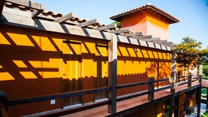 Une pergola en bois avec un motif d’ombres géométriques, un toit en tuiles et un petit espace jardin agrémenté d’un banc et de plantes en pot.