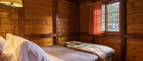 Une pièce de style cabane en bois, avec un lit, une fenêtre avec des rideaux et une lampe fixée au mur.