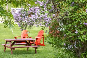 A picnic setup with a table and chairs in a grassy area, surrounded by lush greenery and flowering trees. - Fairmont Creek Property Rentals Timbers Resort (Fairmont Hot Springs)