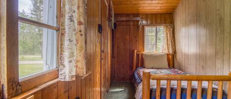 A wooden cabin room with a bed, a window, and a door.