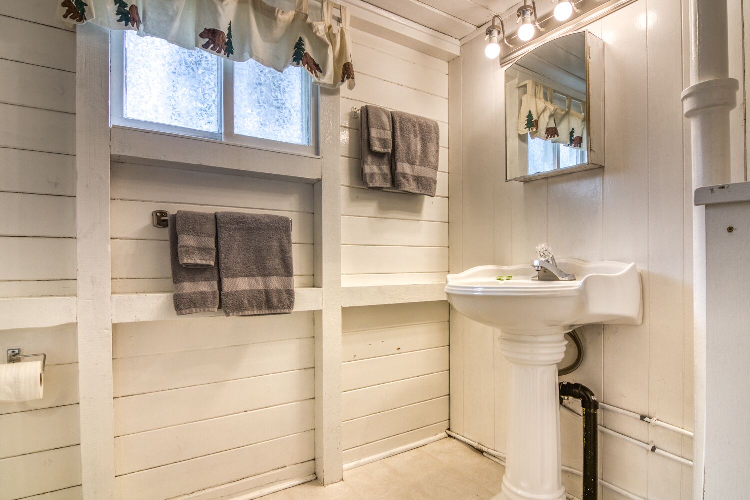 A bathroom with a white sink, two towels, a window with a bear and tree decoration, and a mirror.