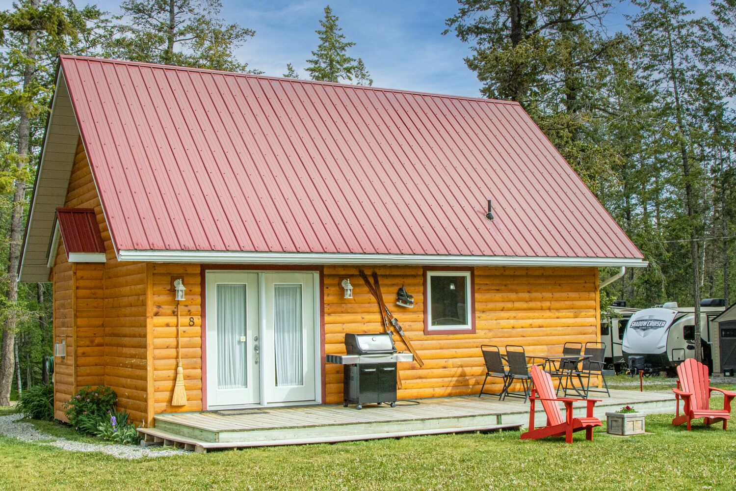 Une cabane en rondins avec un toit rouge, une véranda dotée de meubles d’extérieur et un barbecue.