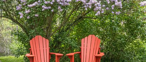 Dos sillas Adirondack rojas en un jardín con un árbol de flores moradas.