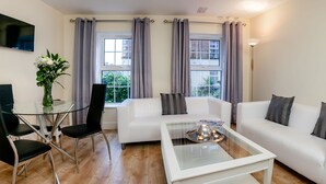Uma sala de estar moderna com um sofá branco, uma mesa de centro de vidro e uma área de jantar com mesa e cadeiras de vidro.