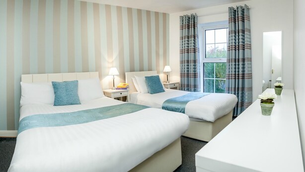 Quarto de hotel com duas camas, uma mesa e janela com cortinas.