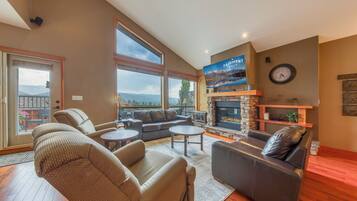 A spacious living room with a fireplace, leather sofas, and large windows offering a view of the mountains.